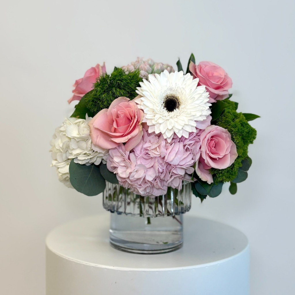 Pretty pink roses, cheery gerbera daisies, fluffy hydrangeas and long-lasting commercial mums, accented with dianthus, trachelium and greens, in a clear glass vase.