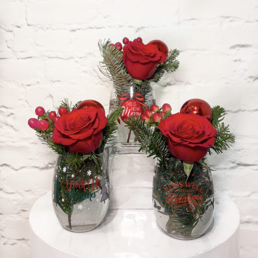 Cup of Cheer flower arrangements with red roses, berries and winter greens in a holiday wine glass.