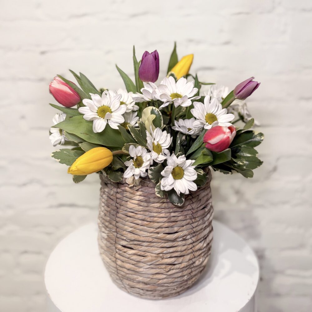 Basket Blooms is a spring flower arrangement full of fresh tulips, daisies and lush greens