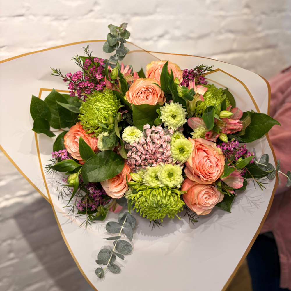 A vibrant mix designed to celebrate Mom in full colour. The Bright Mama Bouquet features soft peach roses paired with lush green disbuds, poms, and commercial mums, accented with delicate alstroemeria and wax flower for a touch of texture and charm. Finished with fresh greenery and beautifully wrapped.