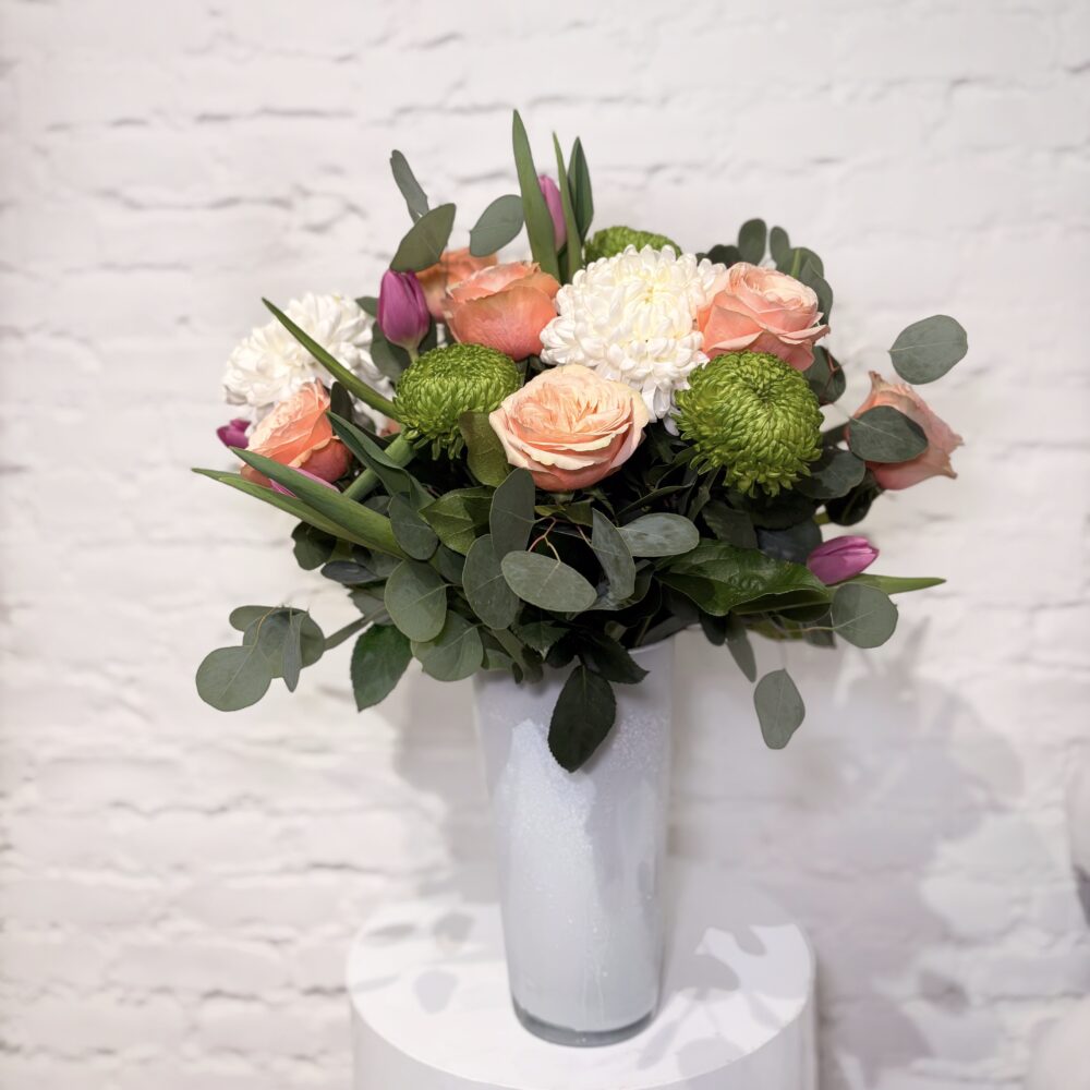 Modern Mother’s Day flower arrangement with roses, tulips, green mums and greenery in glass vase